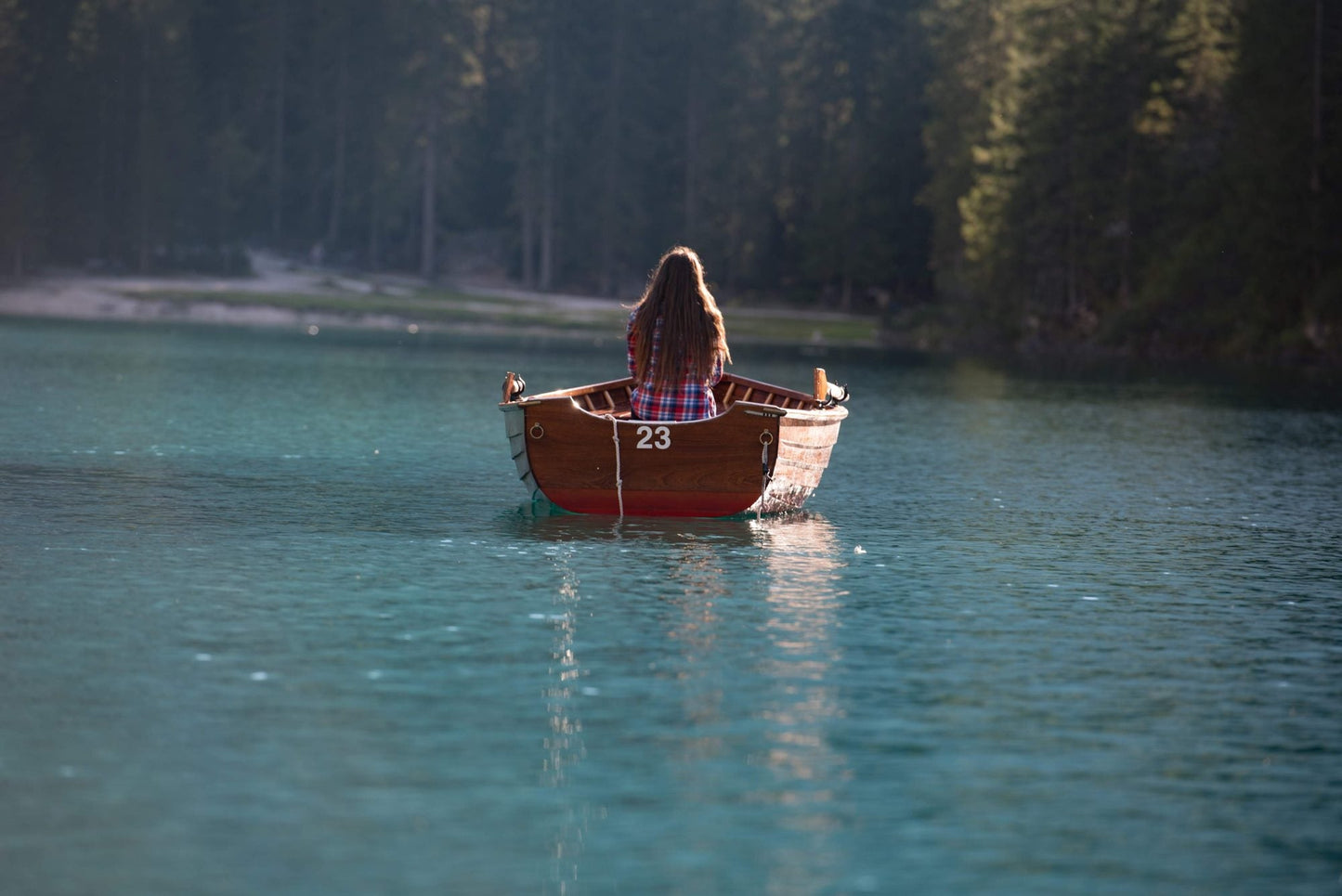 Woman in a wooden rowing boat on the turquoise water of Lago di Braies (Pragser Wildsee), Dolomites