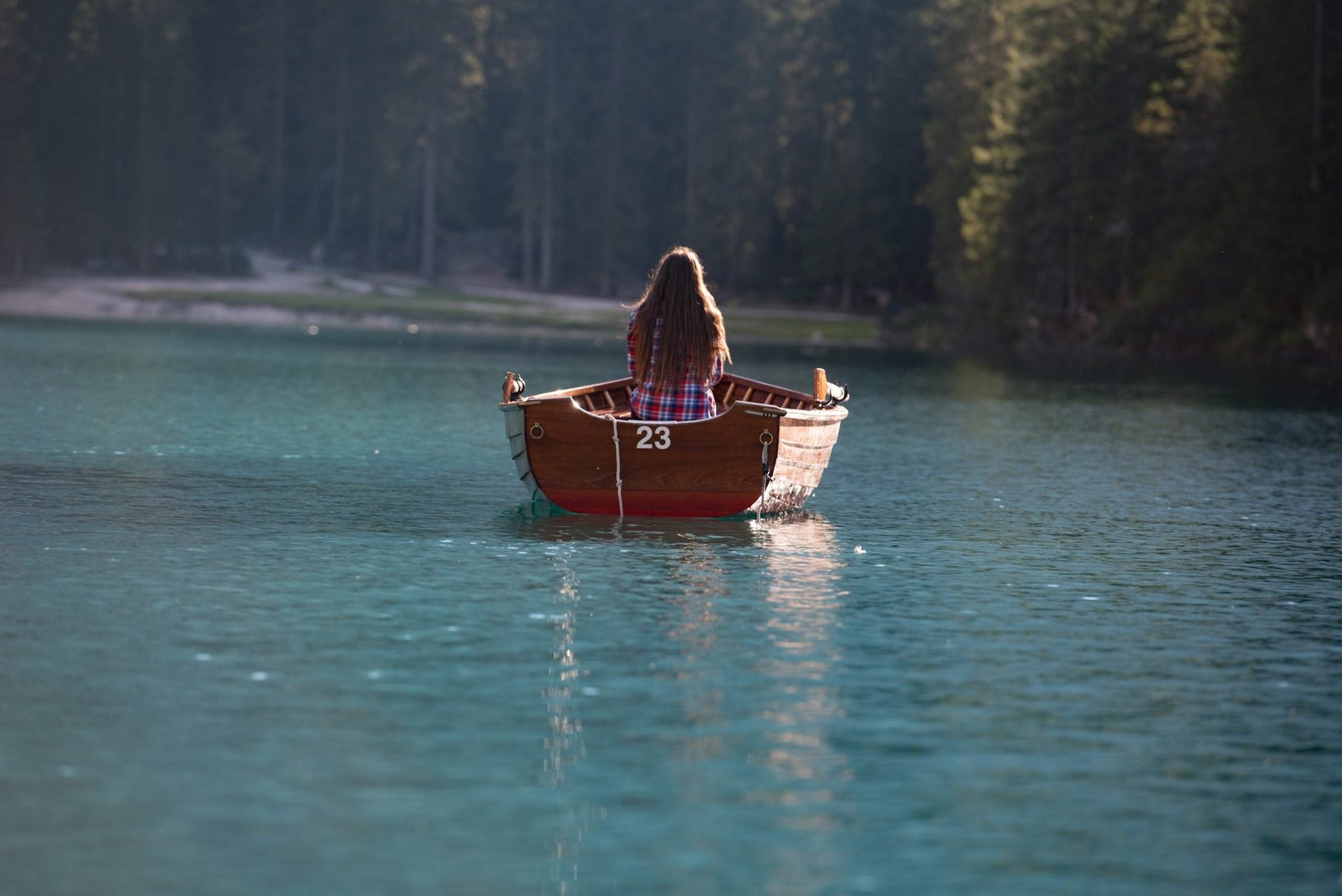 Woman in a wooden rowing boat on the turquoise water of Lago di Braies (Pragser Wildsee), Dolomites