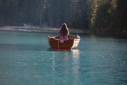 Woman in a wooden rowing boat on the turquoise water of Lago di Braies (Pragser Wildsee), Dolomites